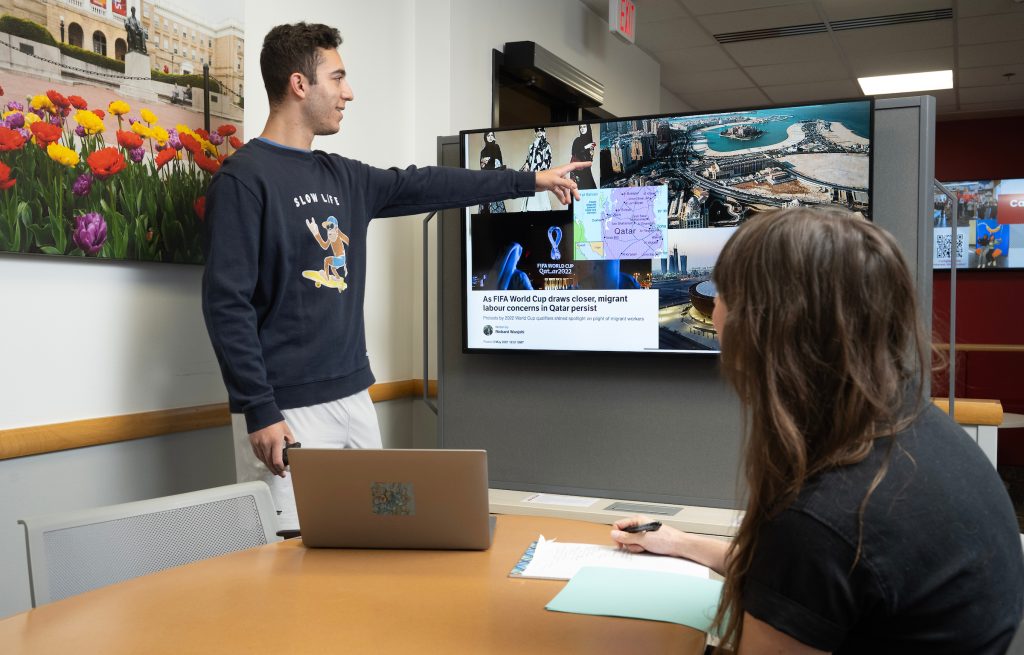 Image of a student pointing at a powerpoint slide and talking while a PWL coach listens