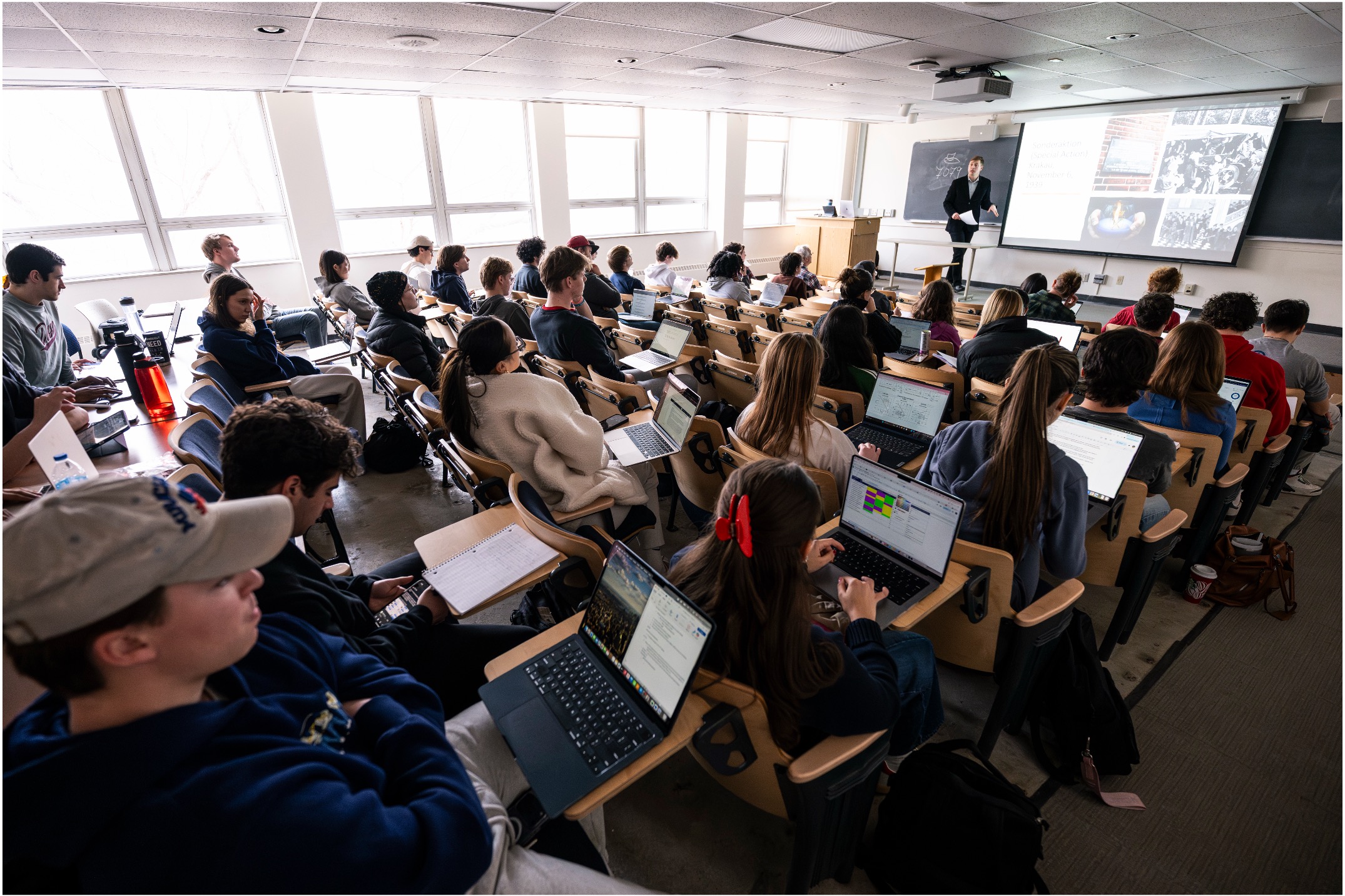 A large class with students looking at an instructor, who is presenting slides